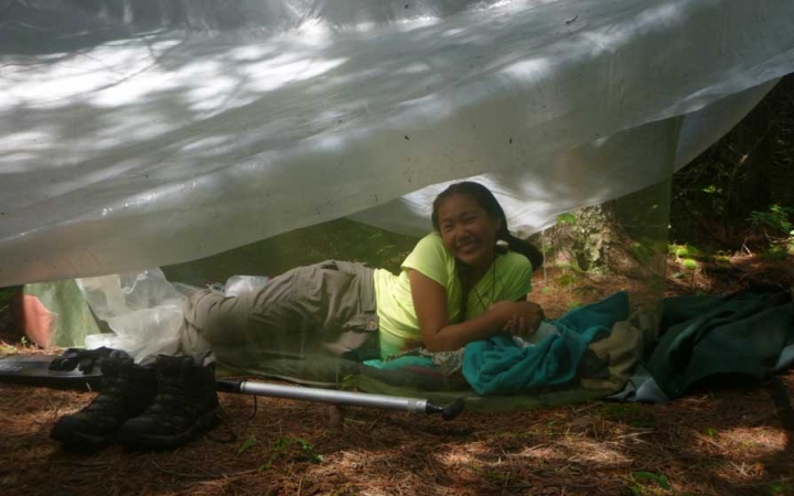 a person smiles from under a tarp shelter on an outward bound course